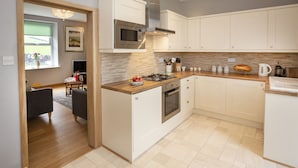 A modern kitchen with white cabinetry, a stainless steel range hood, a built-in oven, and a wooden countertop.