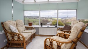 A conservatory with wicker furniture, a view of the countryside, and a radiator.