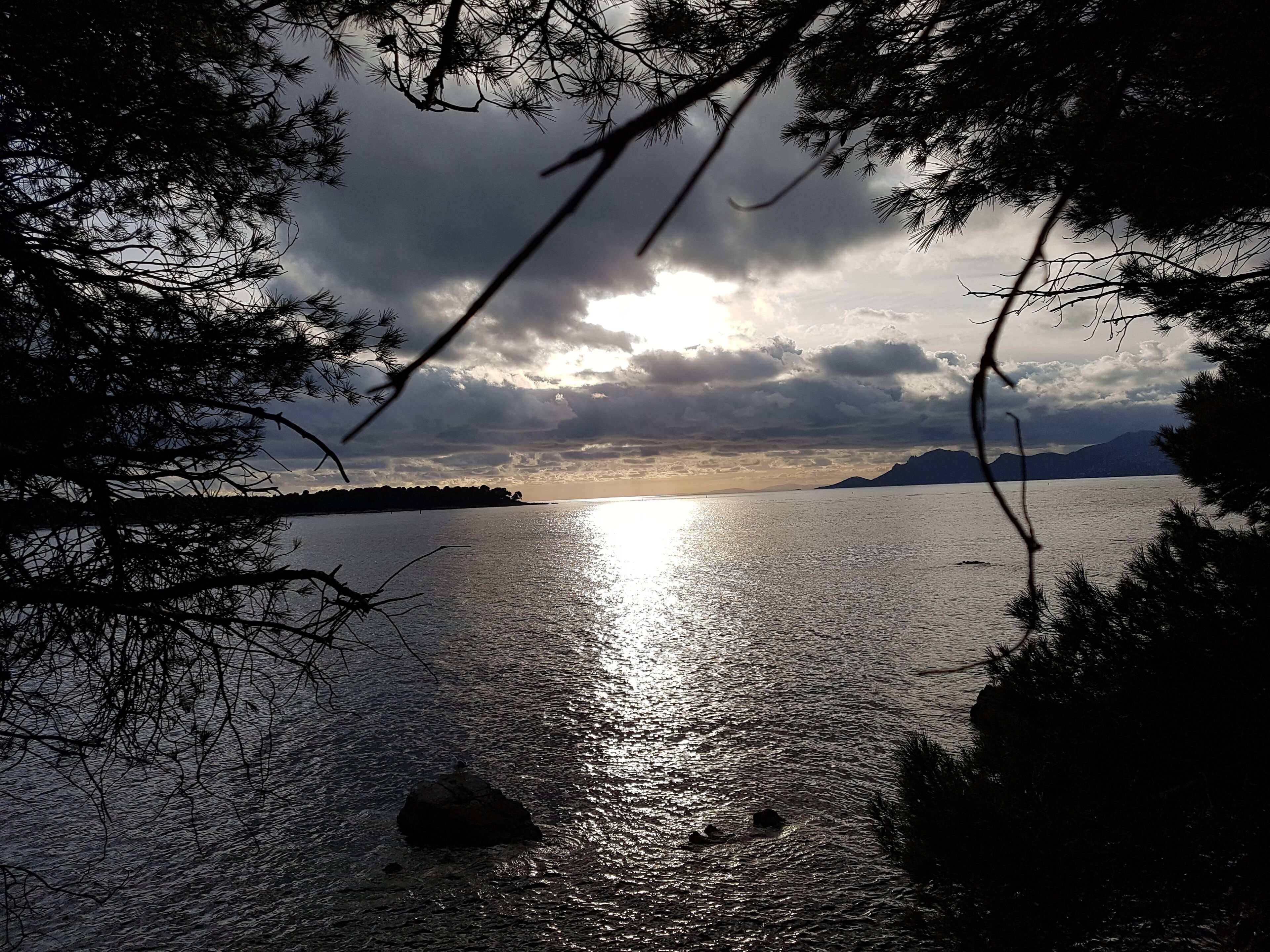 A serene lake with a sunset, surrounded by trees and mountains in the distance.