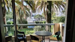 Un balcone con un tavolo rotondo e sedie, affacciato su un giardino con palme.