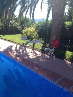 A swimming pool with a tiled edge, surrounded by a patio area with two white chairs and a small table.