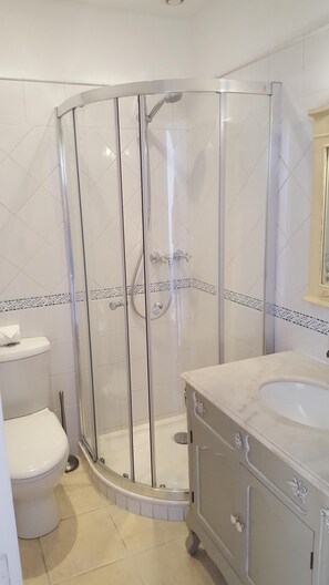 Ett badrum med en dusch som är avskärmad med glasväggar, en vit toalett och ett handfat i marmor.
