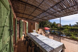 An outdoor dining area with a table and chairs, a covered patio, and a view of a swimming pool.