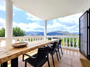 Eine Terrasse mit Holztisch und -stühlen, einem weißen Geländer und Blick auf Berge.