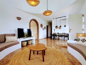 Ein modernes Wohnzimmer mit Fernseher, Sofa, Couchtisch und Essbereich mit Stühlen und Tisch.