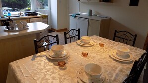 Comedor con una mesa preparada para cuatro, cocina al fondo y ventana con vistas a zonas verdes.