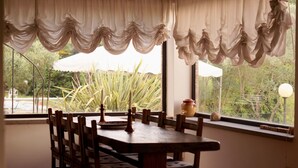 Un comedor con mesa y sillas de madera, una ventana con cortinas y vistas al exterior.