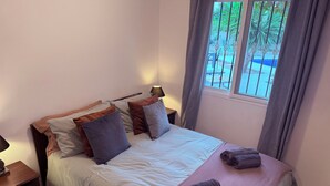 En pænt redt seng med mange puder, et natbord med en lampe og et vindue med gardiner.