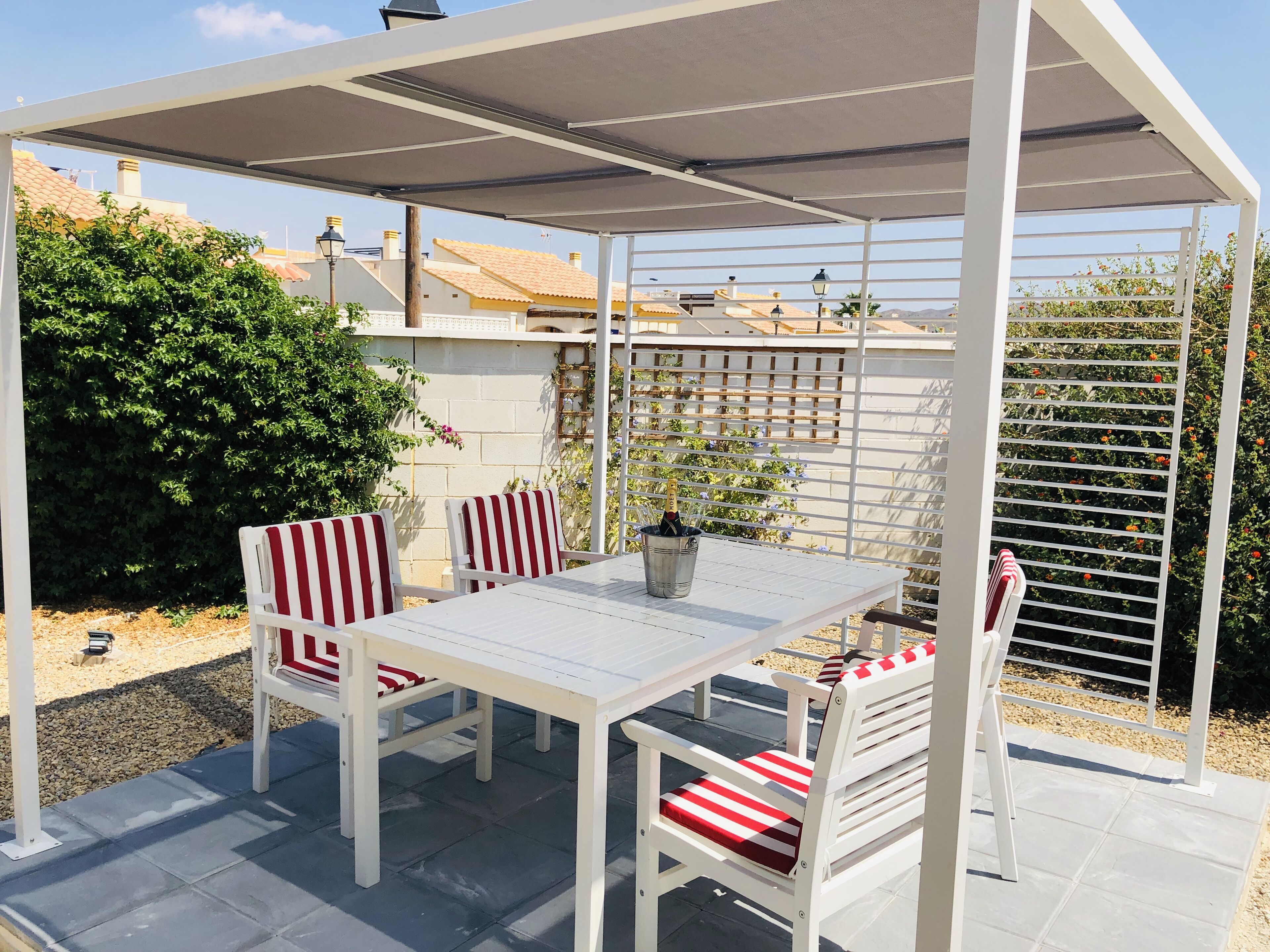 A covered patio area with a table and chairs, a potted plant, and a trellis with climbing plants.