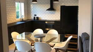 Et moderne køkken med et glasbord, hvide stole, sorte skabe og et sort køleskab.