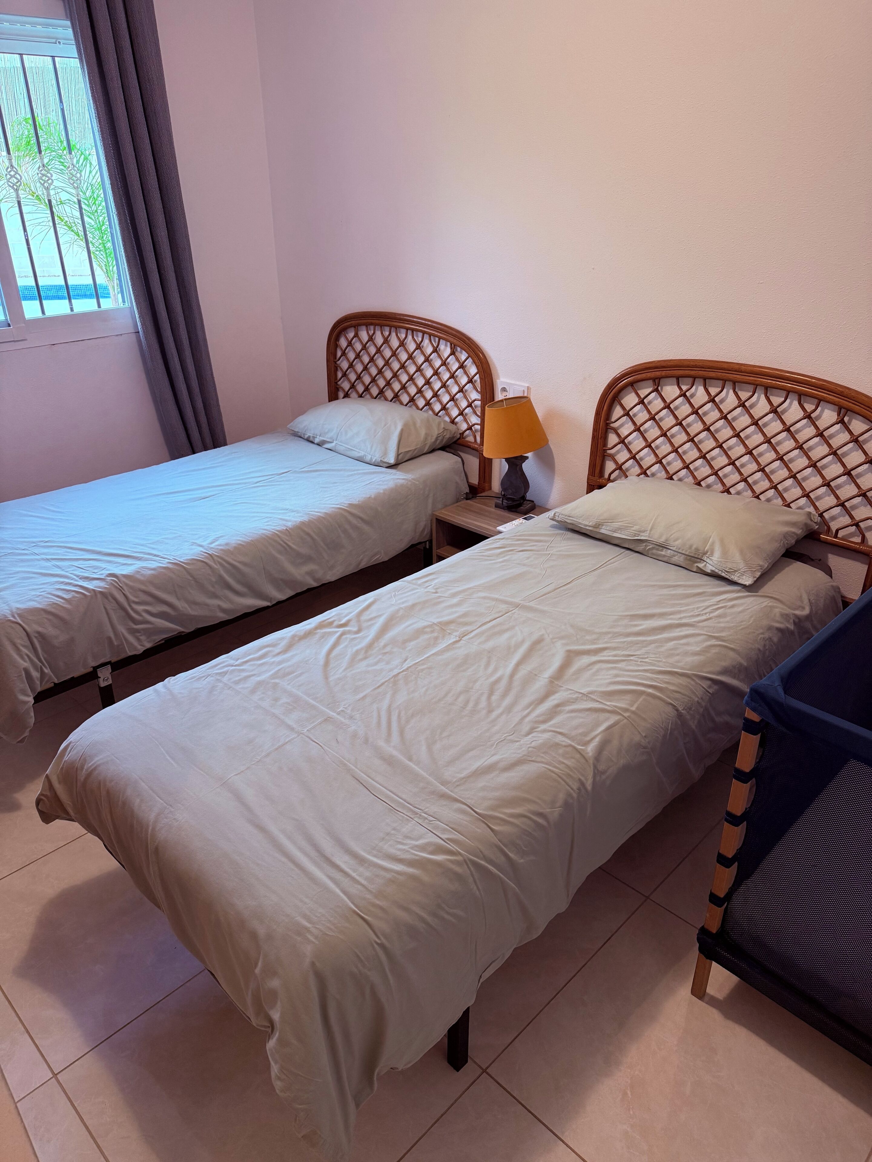 A hotel room with two single beds, a nightstand with a lamp, and a window with curtains.