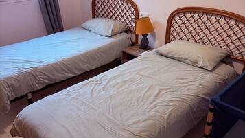 A hotel room with two single beds, a nightstand with a lamp, and a window with curtains.