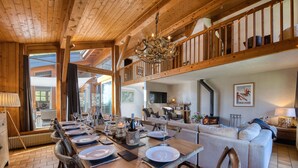 A spacious dining area with a wooden table set for a meal, a high ceiling with exposed beams, and a cozy seating area with a sofa and chairs.