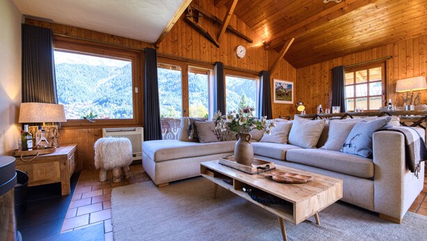 A cozy living room with a wooden ceiling, a sofa, a coffee table, and a view of the mountains.