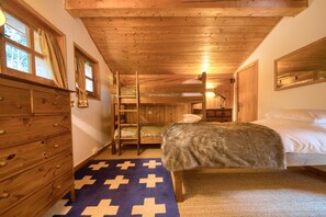 A wooden cabin bedroom with bunk beds, a dresser, and a window with curtains.