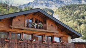 A wooden chalet with a balcony, large windows, and a view of mountains.