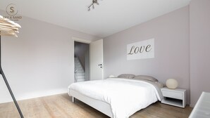 Une chambre à coucher comprenant un lit, une table de chevet, un panneau fixé au mur et un escalier menant à une autre pièce.