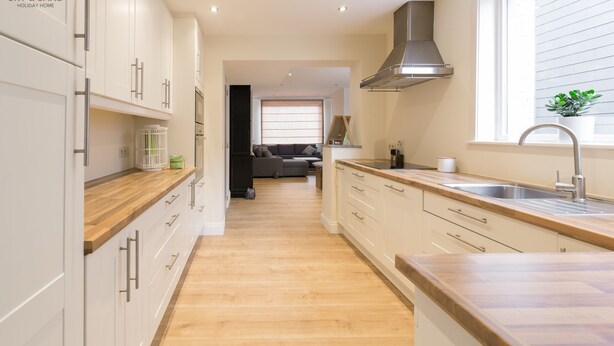 Une cuisine moderne avec des meubles blancs, des plans de travail en bois et une grande fenêtre.