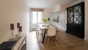 Une cuisine moderne avec des meubles blancs, une table à manger en bois et un meuble noir doté de portes en verre.