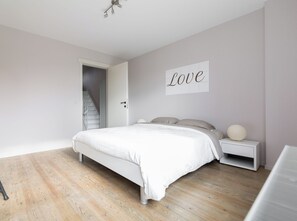 A bedroom with a bed, a nightstand, a wall-mounted sign, and a staircase leading to another room.