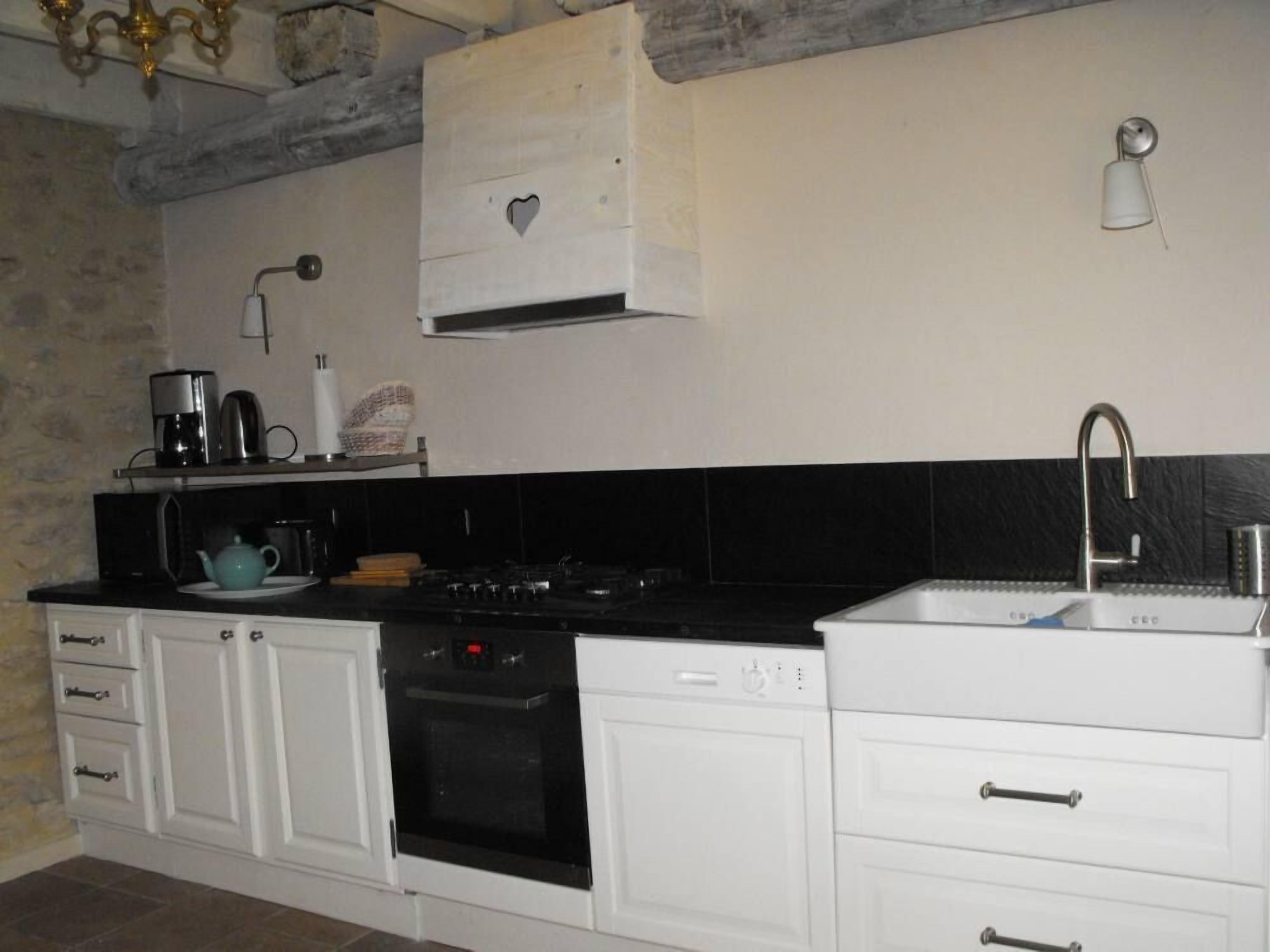 A kitchen with white cabinets, a black countertop, a stove, a sink, and a ceiling light fixture.