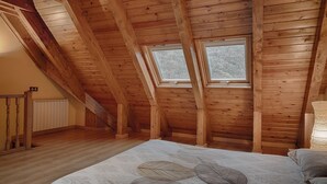 Un dormitorio con vigas de madera, techo inclinado, dos ventanas, un radiador y una cama con colcha estampada con hojas.