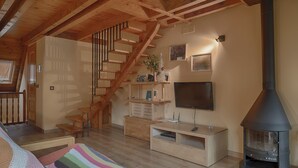 Un dormitorio estilo loft acogedor con una escalera de madera, un televisor, una chimenea y una zona de estar confortable.