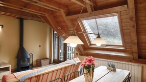 Interior acogedor de una cabaña con techo de madera, un ventanal con vistas al exterior, una chimenea y un comedor con mesa y banco.