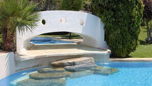 A swimming pool with a white arch bridge, a palm tree, and a well-maintained lawn.