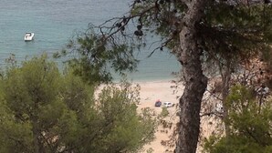 A beach with a boat on the water, trees, and a few scattered items on the sand.