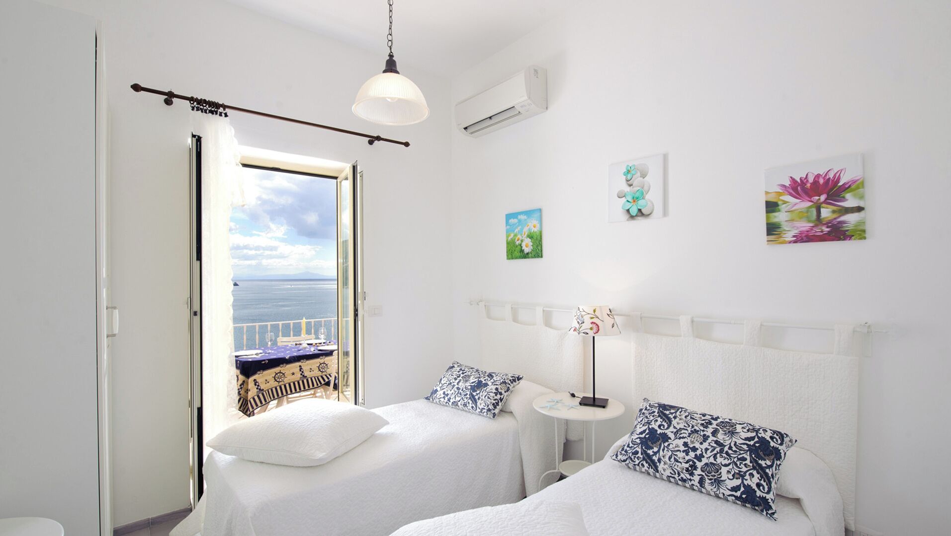 Ein Schlafzimmer mit zwei Betten, Meerblick durch eine offene Tür und Kunstwerken an den Wänden.
