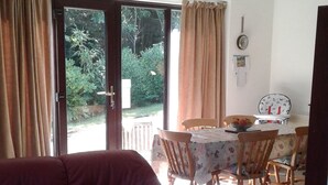A living room with a red leather sofa, a dining table with chairs, and a sliding glass door leading to a garden. - Tranquil Retreat, Two Bedrooms, Two Bathrooms (one en-suite, one shower room) (Hastings)