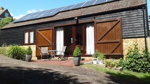 A rustic building with large wooden doors, a patio with outdoor furniture, and solar panels on the roof. - Tranquil Retreat, Two Bedrooms, Two Bathrooms (one en-suite, one shower room) (Hastings)
