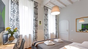 A hotel room with a bed, a desk with a laptop, a chair, a lamp, and curtains. - Grotta Pinta 6 | Spacious and elegant in the heart of Rome (Roma)