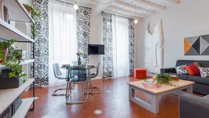 A modern living room with a sofa, a coffee table, and a dining area with chairs and a TV. - Grotta Pinta 6 | Spacious and elegant in the heart of Rome (Roma)