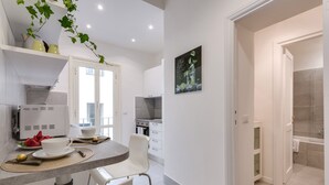 A modern kitchen with white cabinets, a dining area with a table and chairs, and a view into the adjacent bathroom. - Grotta Pinta 6 | Spacious and elegant in the heart of Rome (Roma)