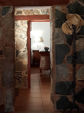 A stone-walled hallway leading to a room with a wooden cabinet and a lamp.