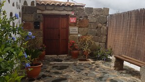 Um edifício de pedra com porta de madeira, plantas em vasos e uma placa com o nome 