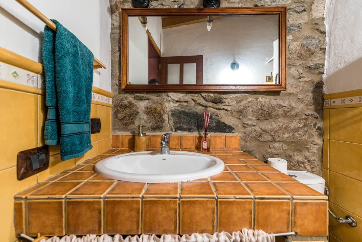 A bathroom with a stone wall, a white sink, and a mirror above it.