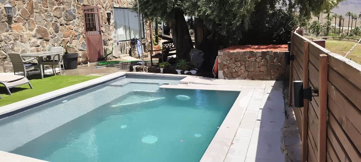 Una piscina rectangular con un muro de piedra y una cerca de madera en un lado.