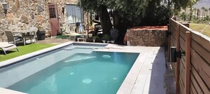 A rectangular swimming pool with a stone wall and wooden fence on one side.