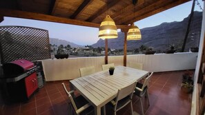 An outdoor patio with a wooden table and chairs, a grill, and potted plants.