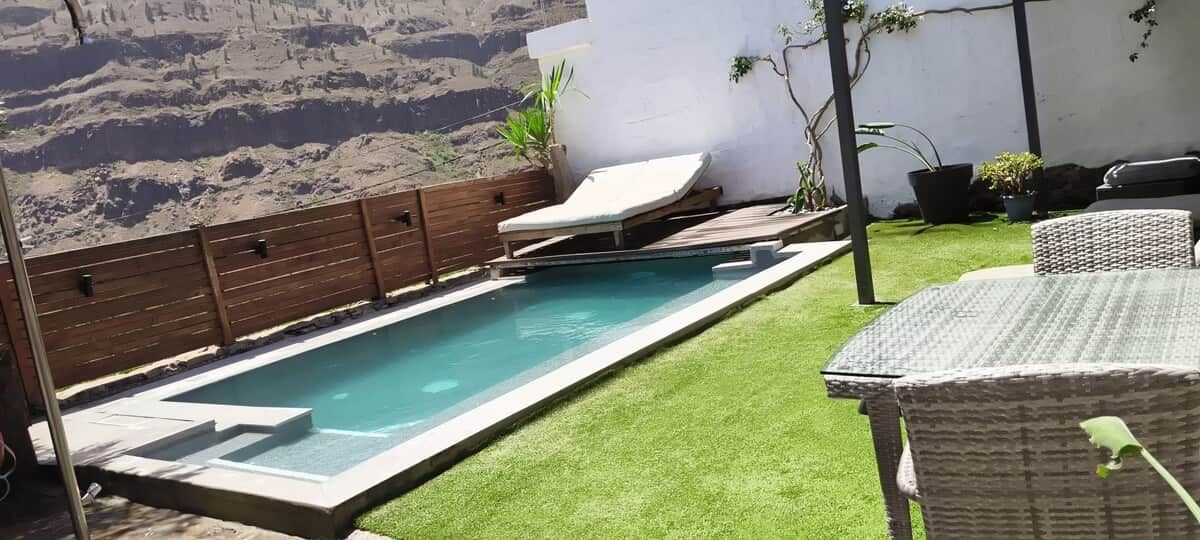 Una piscina con bordo in legno e lettini, circondata da un muro bianco e affacciata su un paesaggio montuoso.