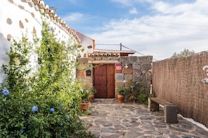 A stone pathway leading to a wooden door, surrounded by potted plants and a stone wall.