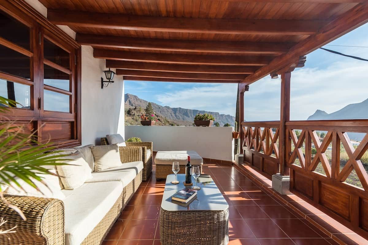 A covered outdoor seating area with a sofa, a table, and a view of mountains.