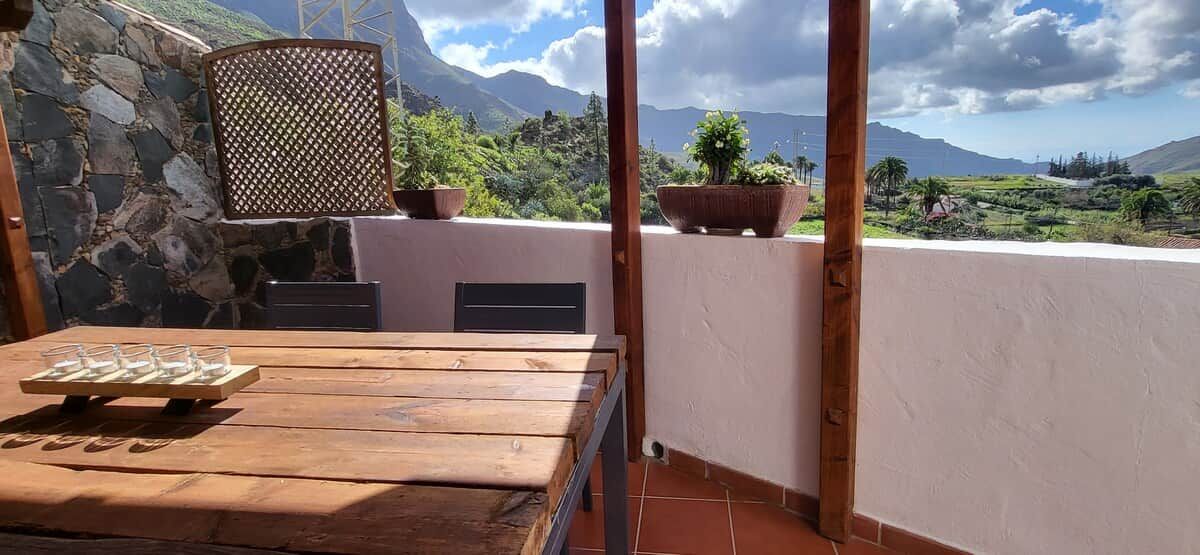 Una mesa de madera con un juego de vasos, una pared de piedra y vistas a un paisaje montañoso.