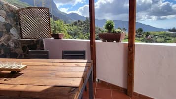 Una mesa de madera con un juego de vasos, una pared de piedra y vistas a un paisaje montañoso.