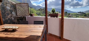 A wooden table with a glass set, a stone wall, and a view of a mountainous landscape.