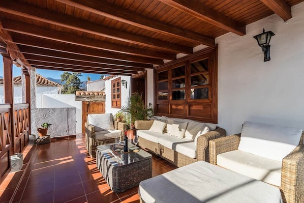 An outdoor patio with wicker furniture, a stone wall, and a view of buildings in the background.
