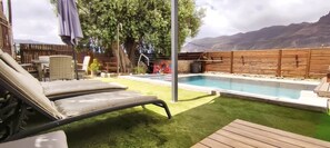 A backyard with a swimming pool, a wooden deck, and a lounge chair.
